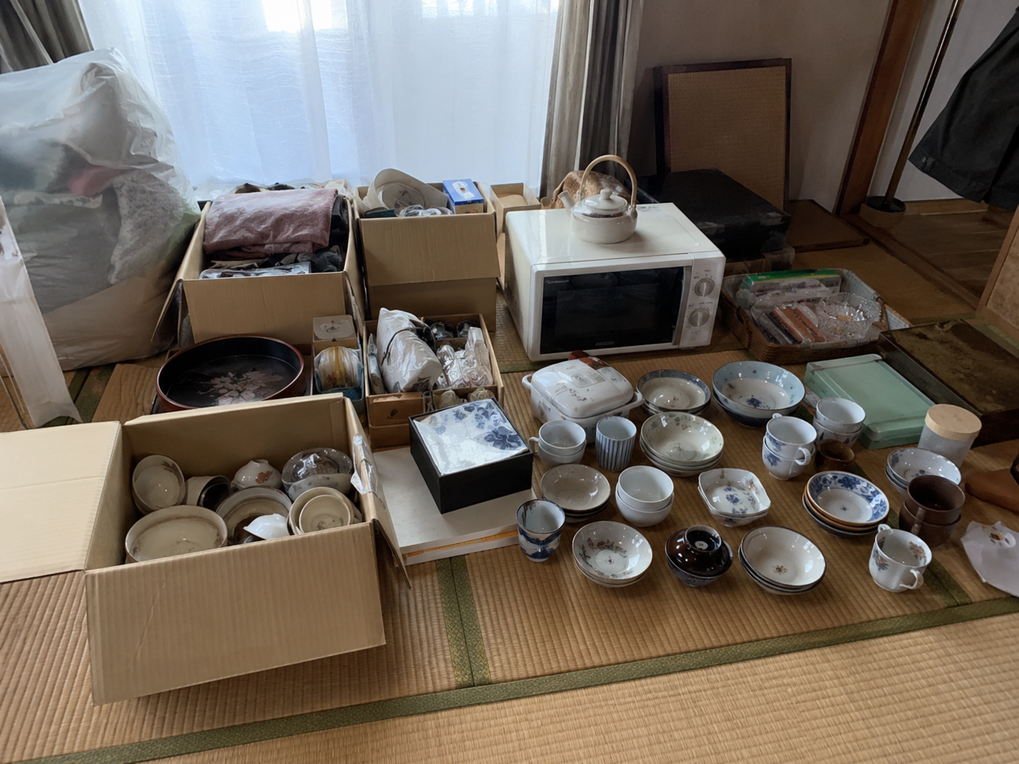 遺品整理／空家整理の現場写真。段ボールに詰められた品々、まだ使える家電や食器が並んでいる様子