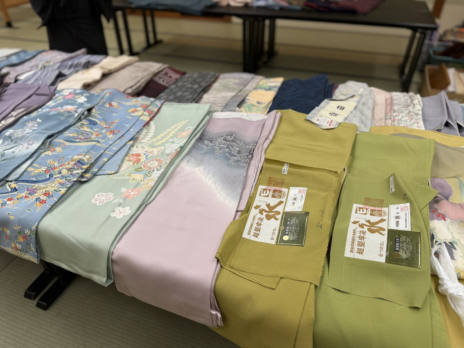 長机に並ぶ淡い色合いの着物や帯。一部に品質表示の証紙が付いている前回会場の様子