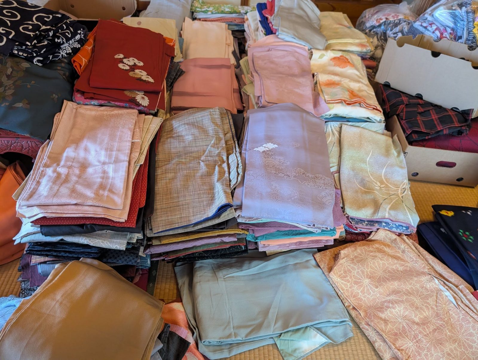 淡い色からはっきりした色まで、折りたたまれた着物や帯が何段にも積まれている様子