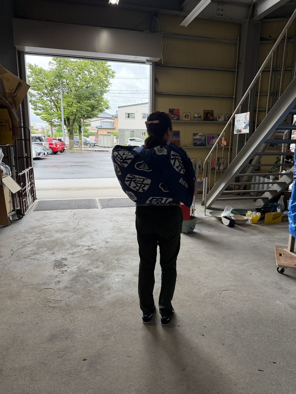 NIIGATA BASEの法被を着たスタッフが、丸めたブルーシートを抱えて開いたシャッターの前に立つ片付けの様子
