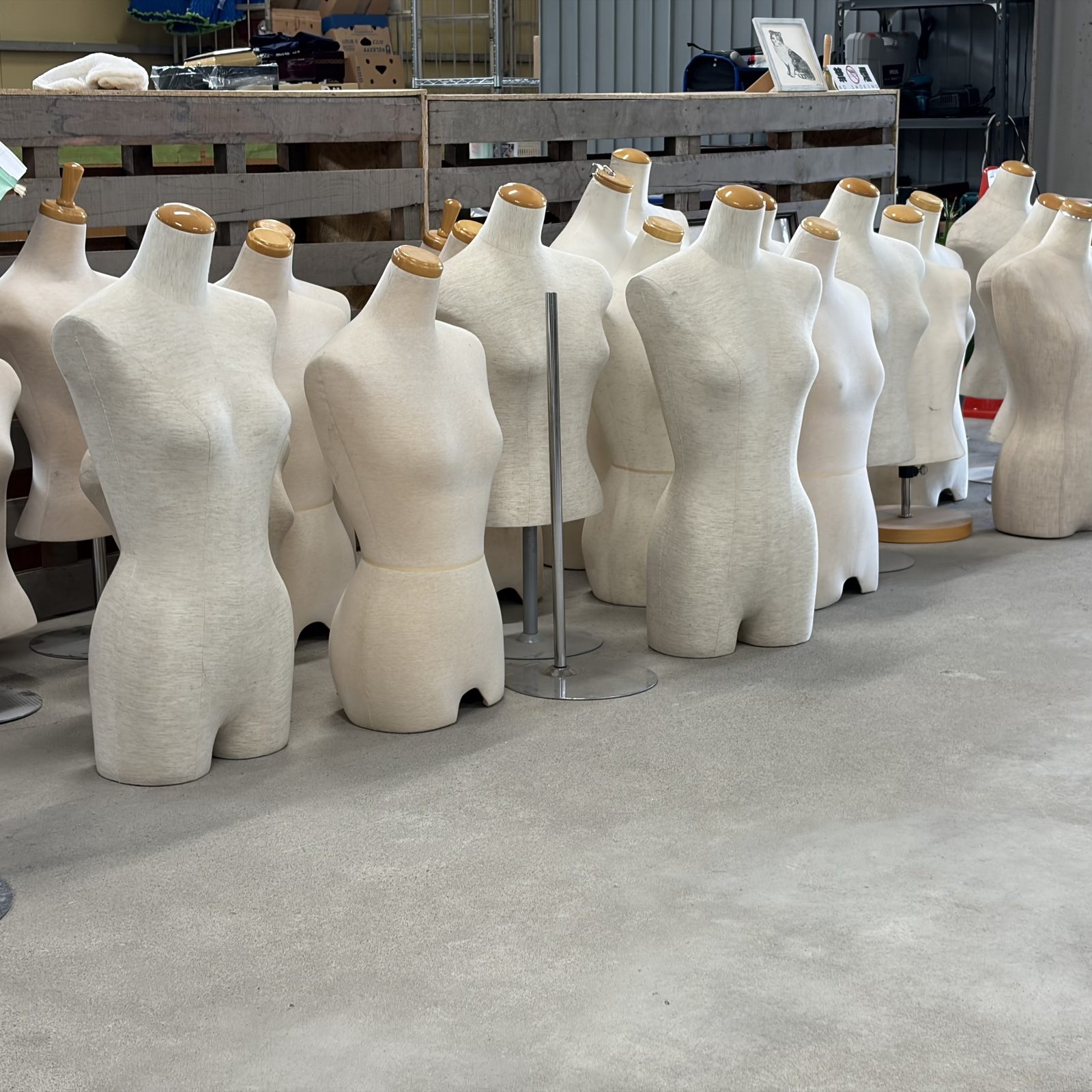 金属スタンドと木製ネックトップが付いた、生成り色の布張りマネキン（トルソー）が一列に並ぶ様子
