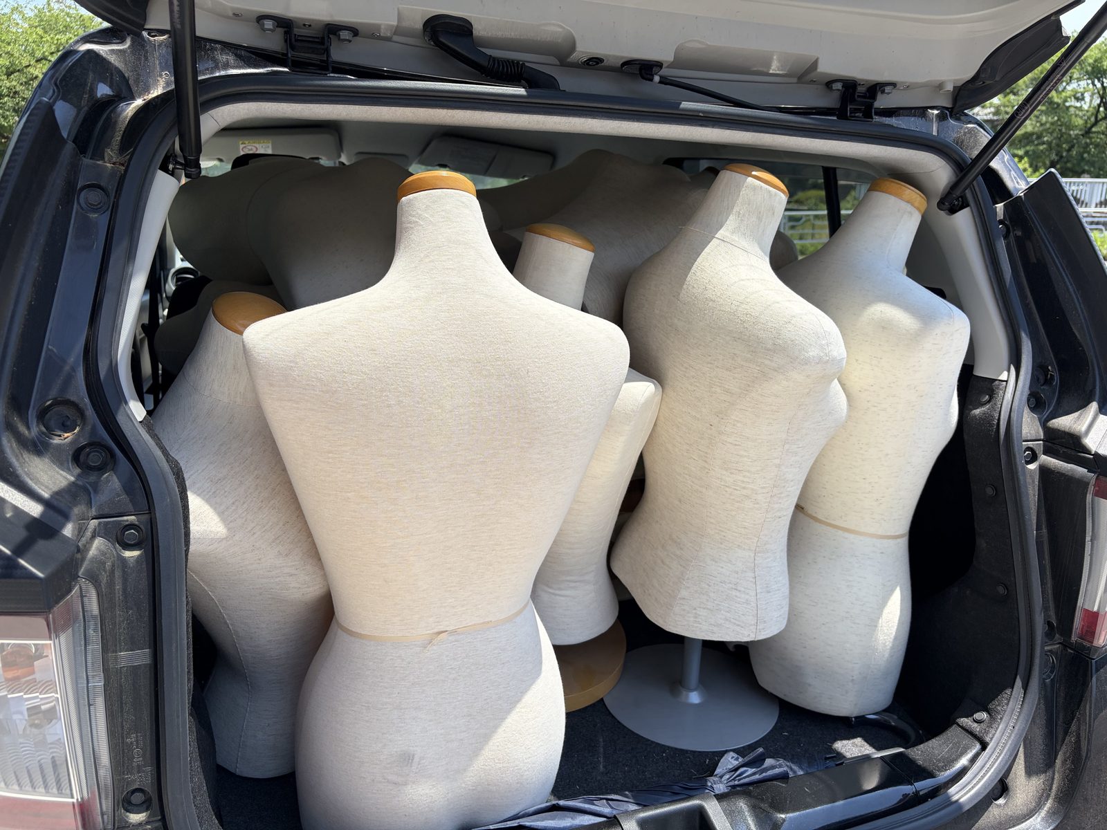 開いたハッチバックの荷室いっぱいに、生成り色の布張りマネキン（トルソー）が積み込まれている様子