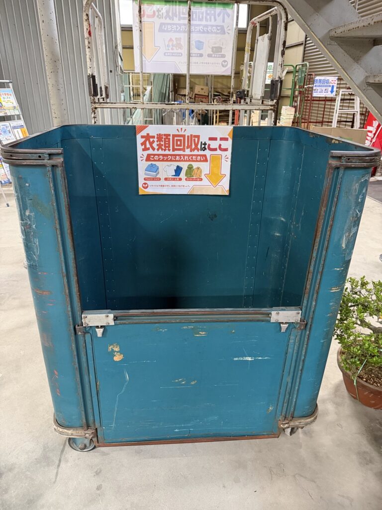 「衣類回収はここ　このラックにお入れください」と書かれた紙が貼られた、青い大きな回収ボックス。