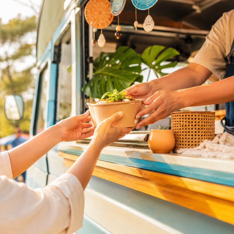 キッチンカーのイメージ。窓口で料理の入ったカップを手渡ししている。