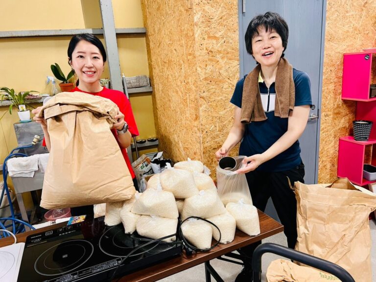 袋詰めされた品物を手にした二人が笑顔でポーズをとっている。