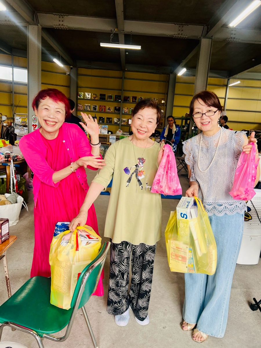 来場者3人が、たくさんの買い物袋を手に笑顔で並んでいる。