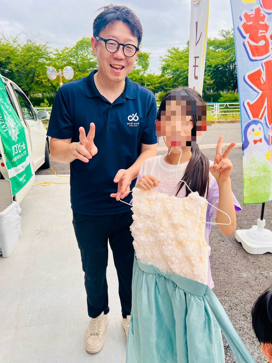 and・endのスタッフと子どもが、ハンガーにかけた洋服を手に笑顔でポーズをとっている。