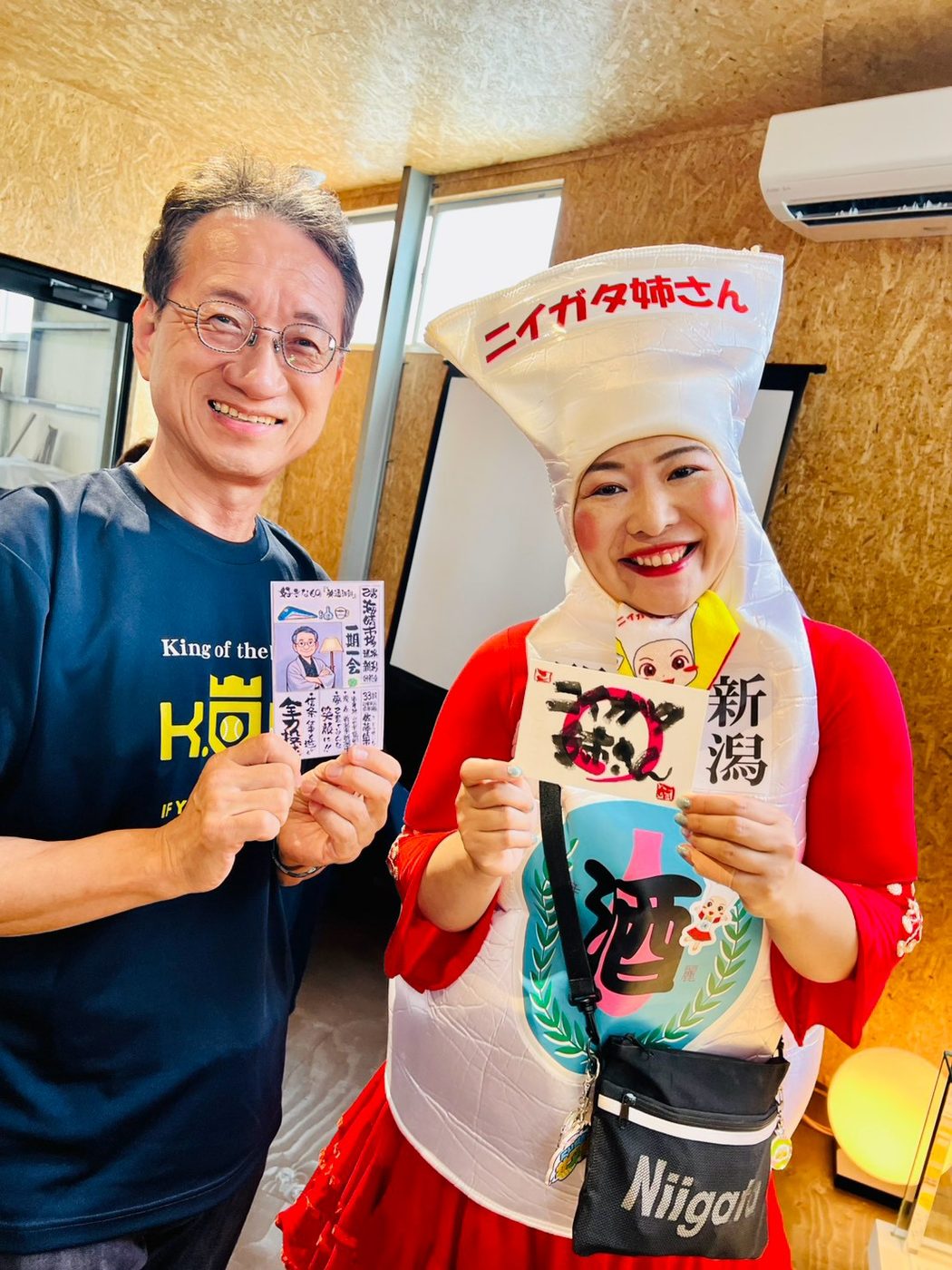 ニイガタ姉さんと男性が、縁日祭のチラシを持って笑顔で並んでいる。