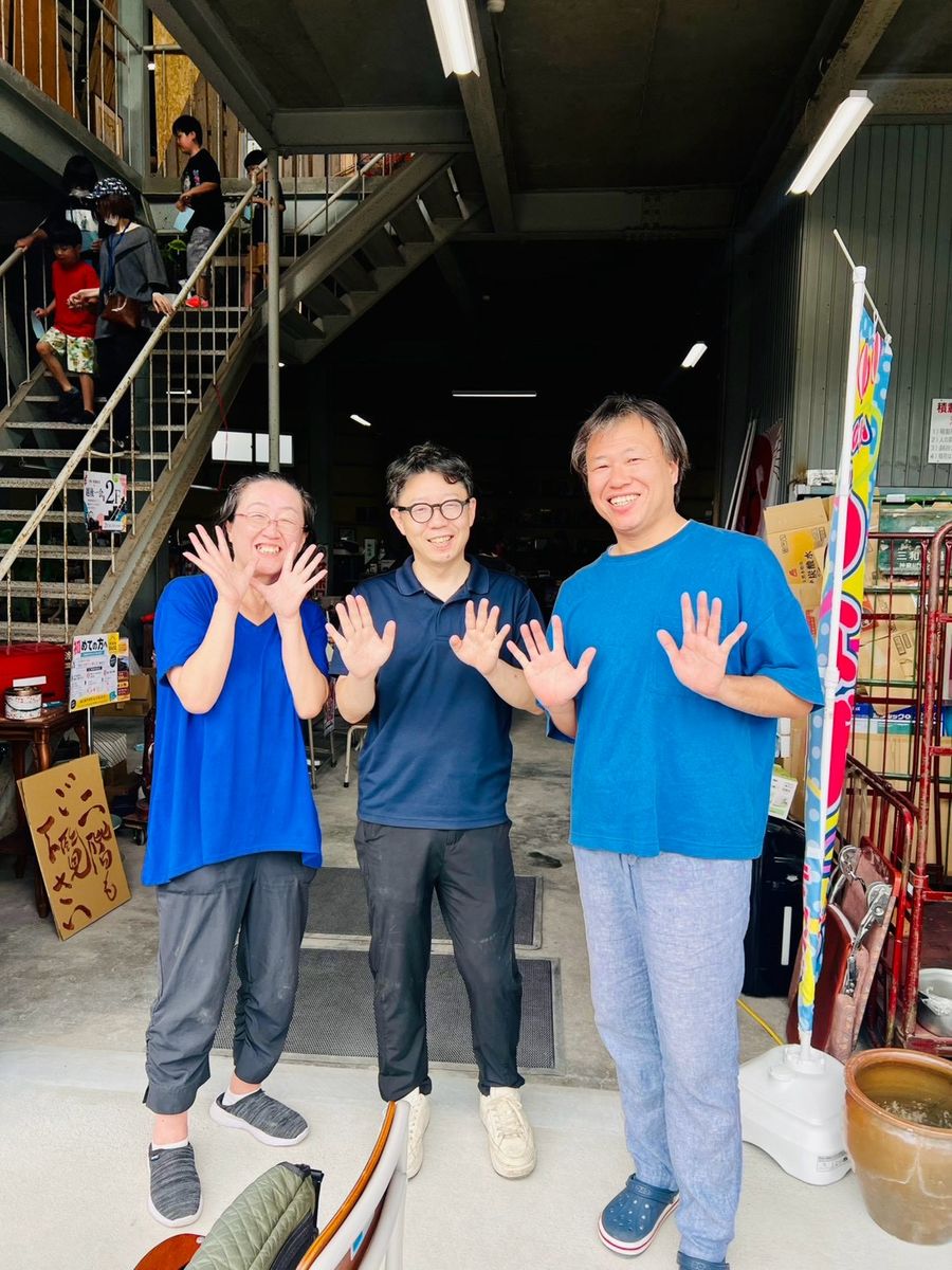 スタッフ3人が、会場の入口で手を振って笑顔でポーズをとっている。