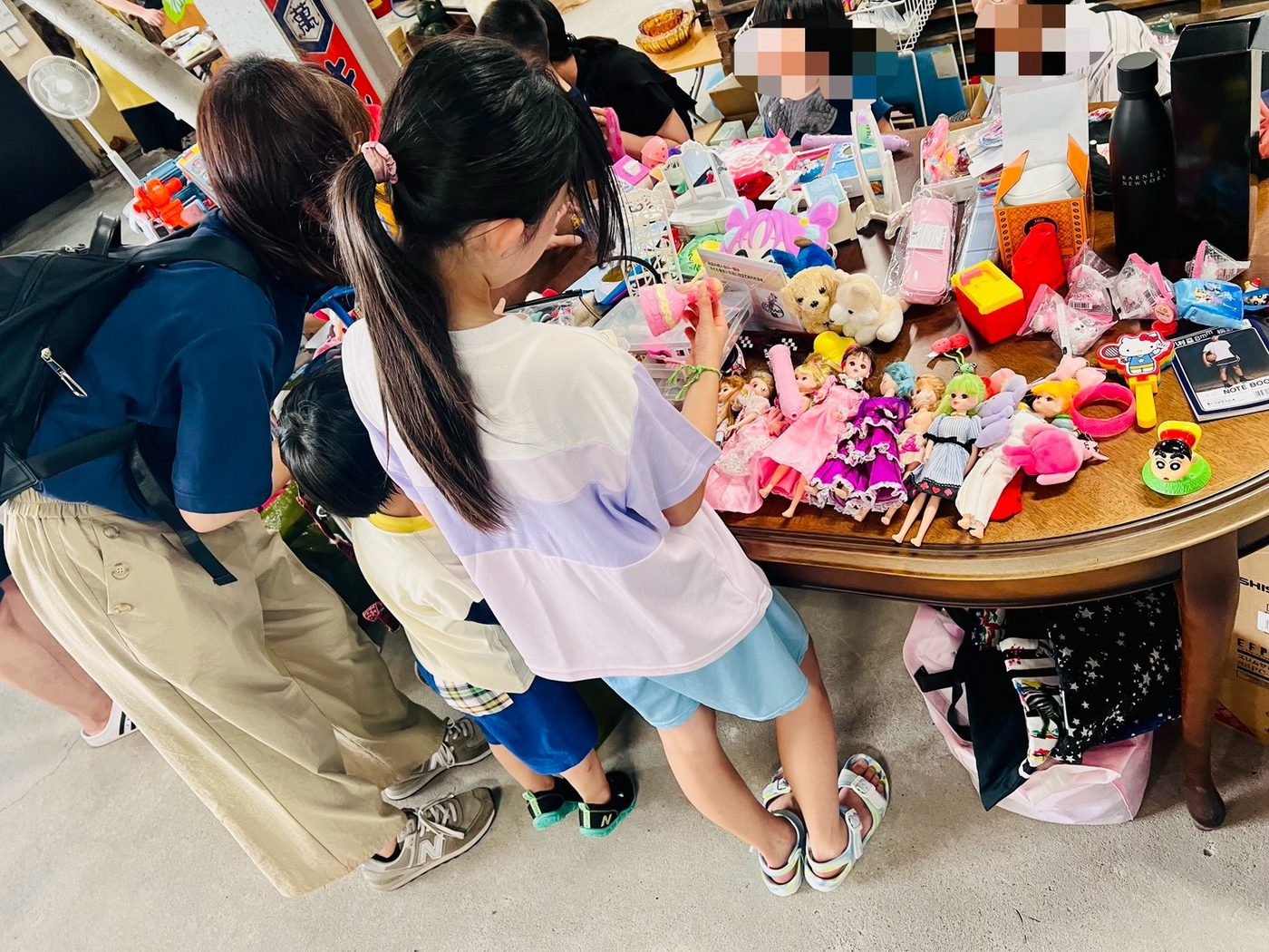 おもちゃやぬいぐるみが並んだテーブルで、子どもたちが夢中で品物を選んでいる。