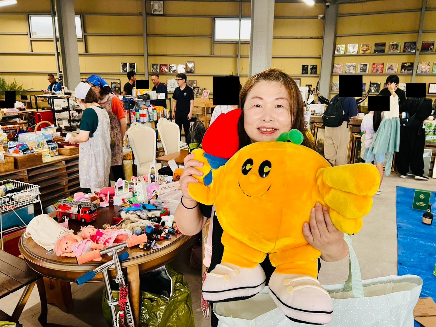 おもちゃコーナーで、黄色い大きなぬいぐるみを両手で抱えて笑顔の来場者。