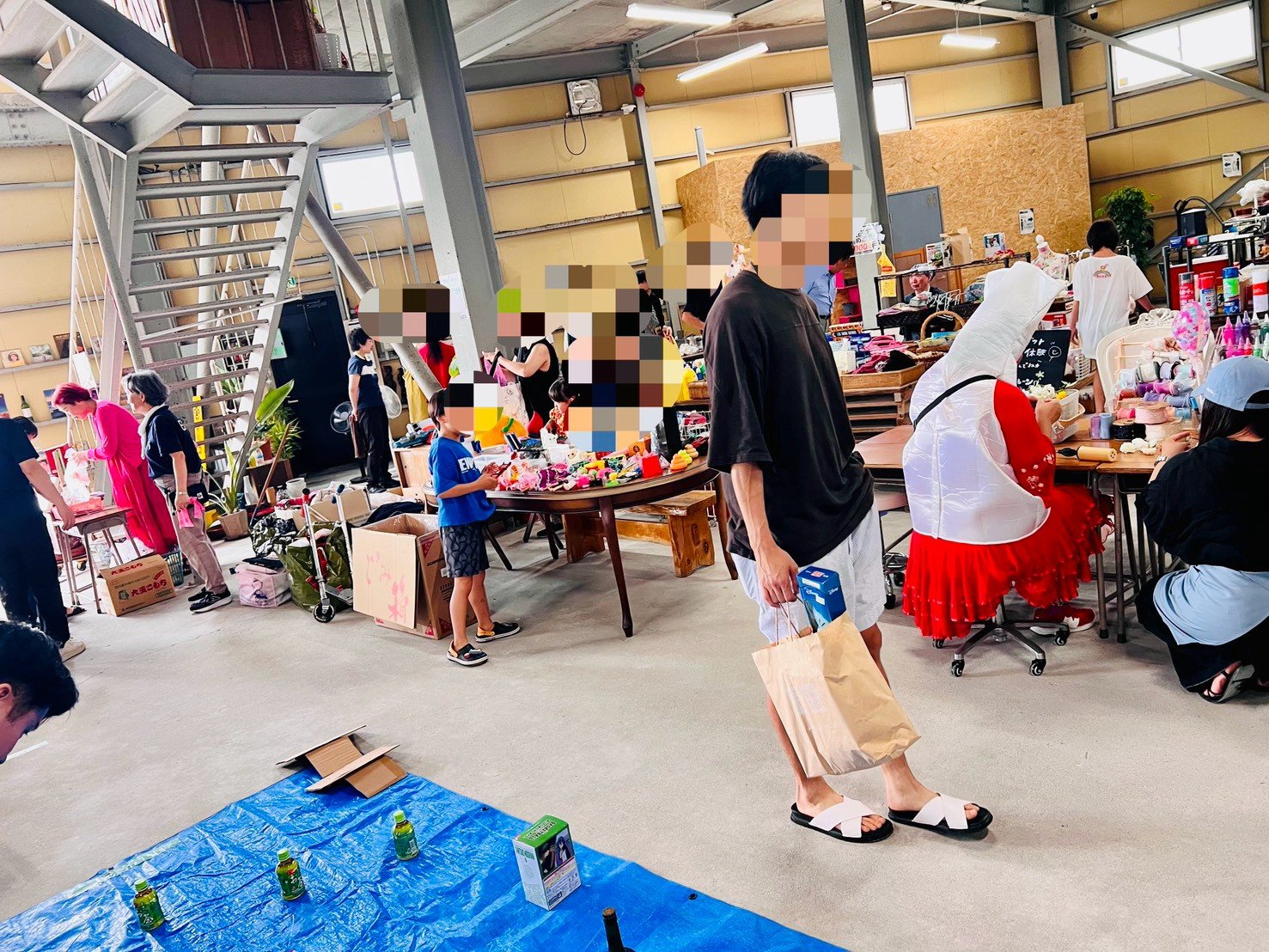 縁日祭の会場。ブルーシートや机の上に日用品や雑貨が並び、来場者が品物を見て回っている。
