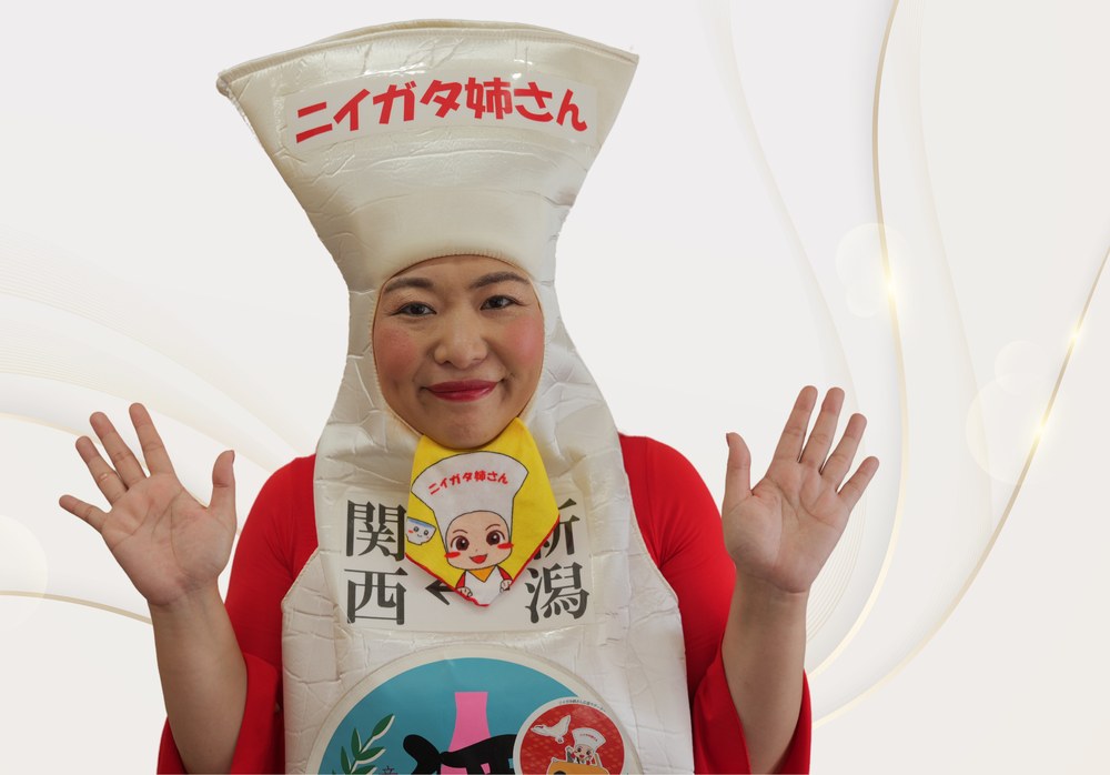 新潟県の非公認PRキャラクター「ニイガタ姉さん」が、徳利のコスチューム姿で両手を広げて笑顔で迎える上半身の宣材写真。