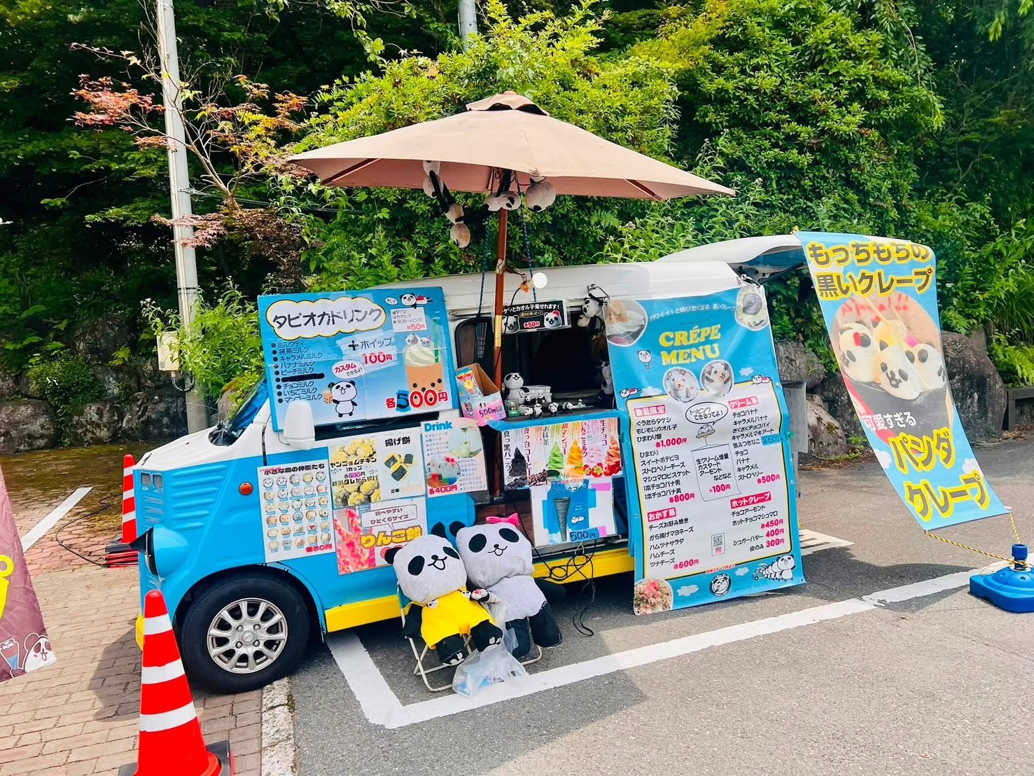 水色のキッチンカーに「もっちもちの黒いクレープ パンダクレープ」の幟が立ち、パンダのぬいぐるみとクレープのメニュー表が並んでいる。