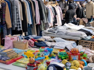 ハンガーに掛かった洋服の手前に、食器やおもちゃ、雑貨が並んだフリーマーケットの台。