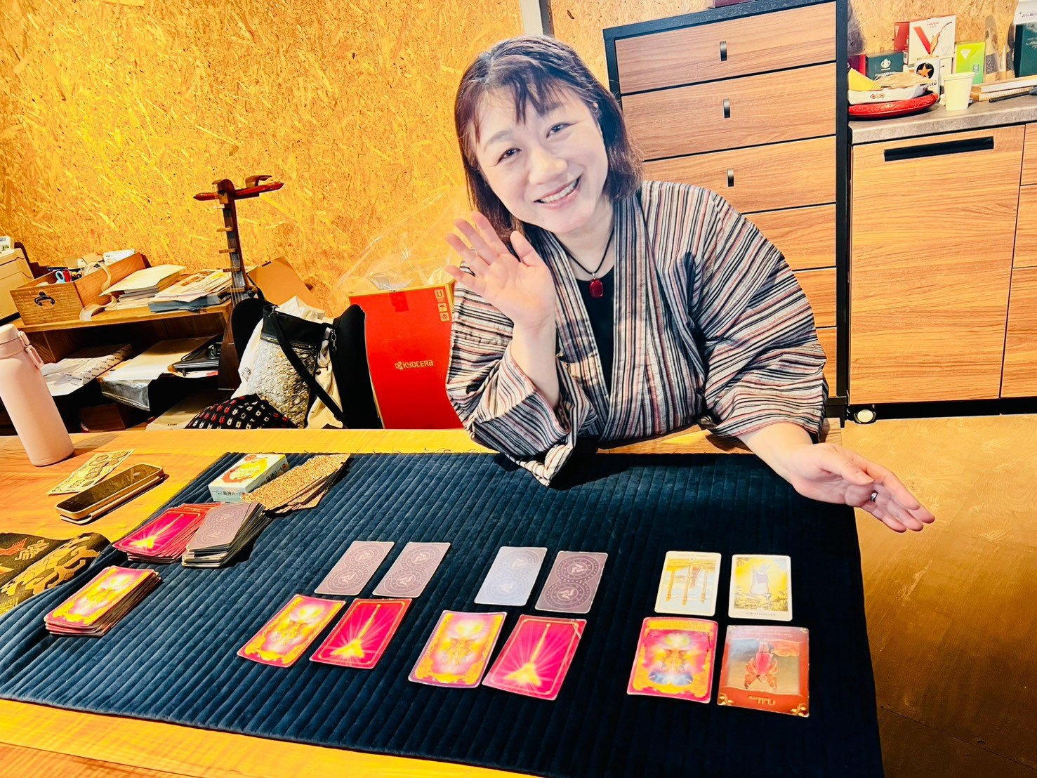 机の上にカードを並べ、和装の女性が笑顔で手を添えている。