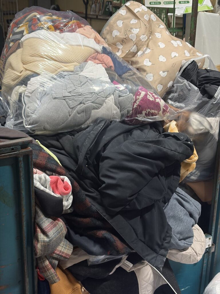 ニイガタベースの店内の衣類回収ボックスに、袋に入った服や毛布、コートがたくさん入っている。
