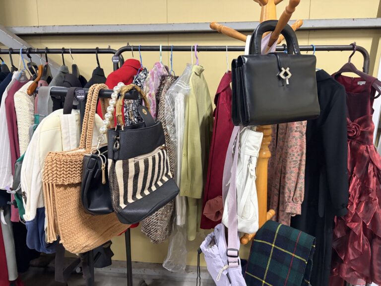 ラックに掛かった服の手前に、かごバッグや黒いハンドバッグ、ストライプのトートバッグが下がっている。