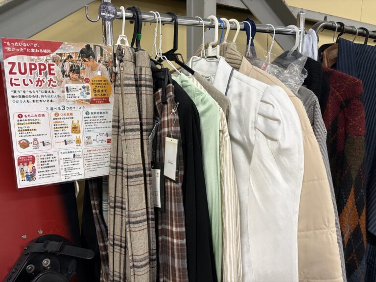 チェックのジャケットや白いブラウス、ベージュのコートが掛かったラックと、ZUPPEにいがたの案内ポスター。